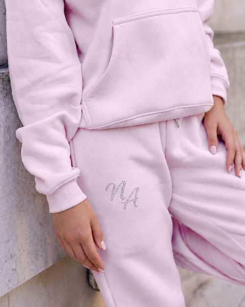 Pink Niamh Avenue cuffed joggers featuring a sparkling crystal rhinestone NA logo on the thigh, styled with a matching black hoodie for a luxury casual look.
